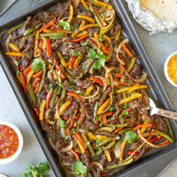 Overhead closeup view of cooked sliced beef, peppers and onions in a sheet pan.