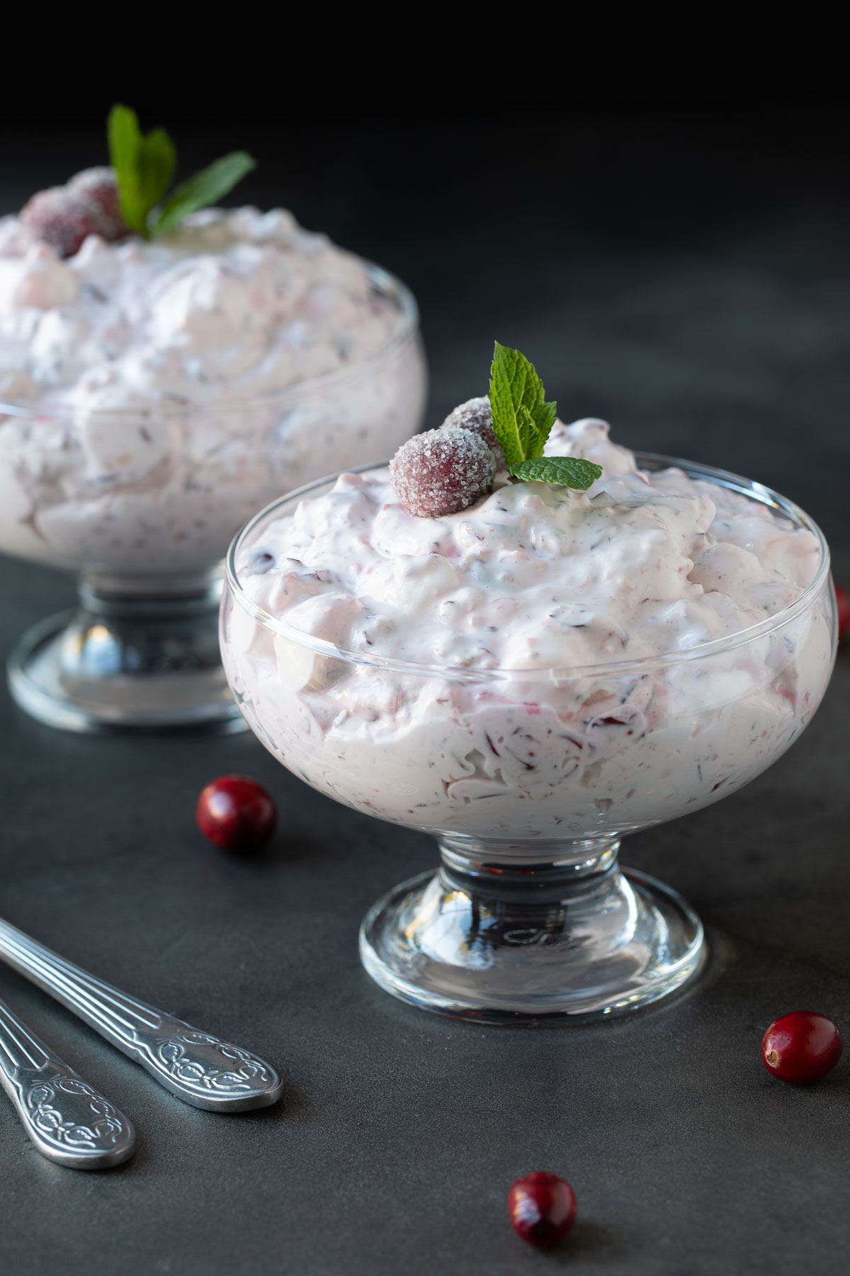 Cranberry fluff salad in two glass dessert bowls on a dark surface.