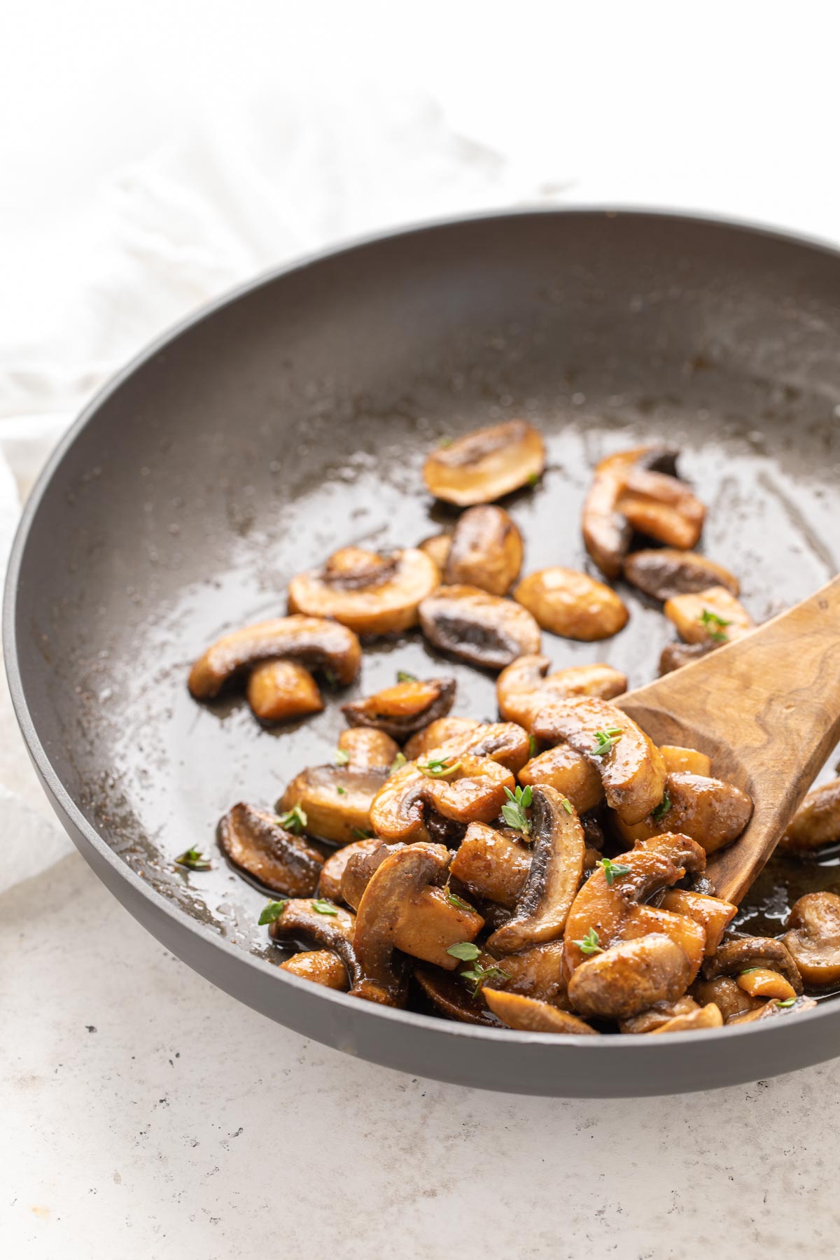 Closeup view of a wooden spoon spooning sauteed mushrooms in a skillet.