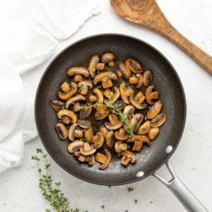 Overhead view of sauteed mushrooms garnished with fresh thyme in a skillet.