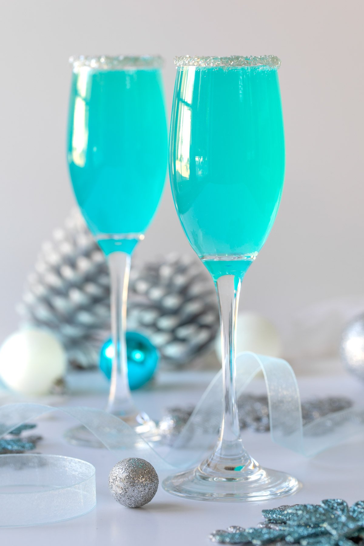 Two tiffany blue mimosas in champagne flutes rimmed with pearlized sugar.