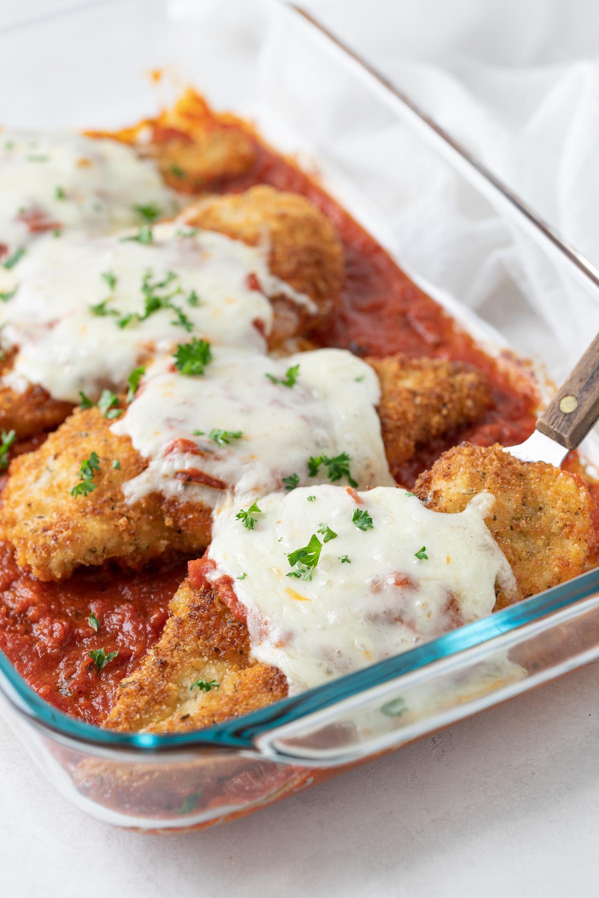 Closeup view of chicken parmesan in a baking dish with a server.