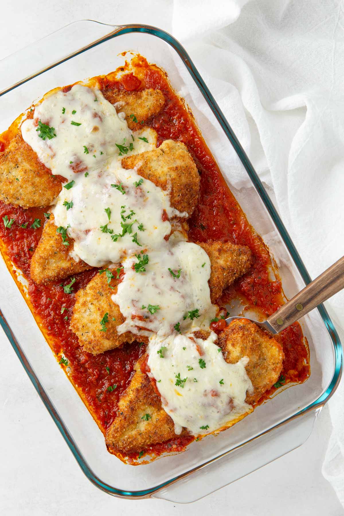 Overhead view of chicken parmesan in a glass baking dish with a server.
