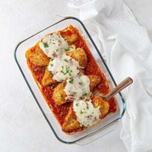 Overhead view of chicken parmesan in a baking dish by a white napkin.