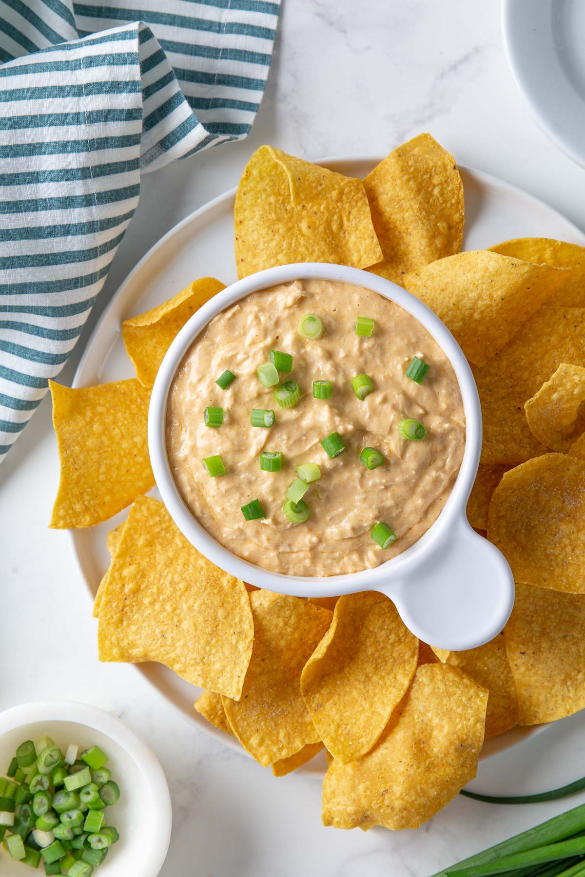 Overhead view of a bowl of chicken enchilada dip on a plate with tortilla chips.