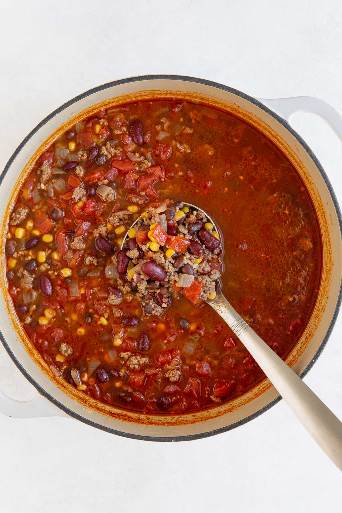 Overhead view of a ladle ladling taco soup from a white Dutch oven.