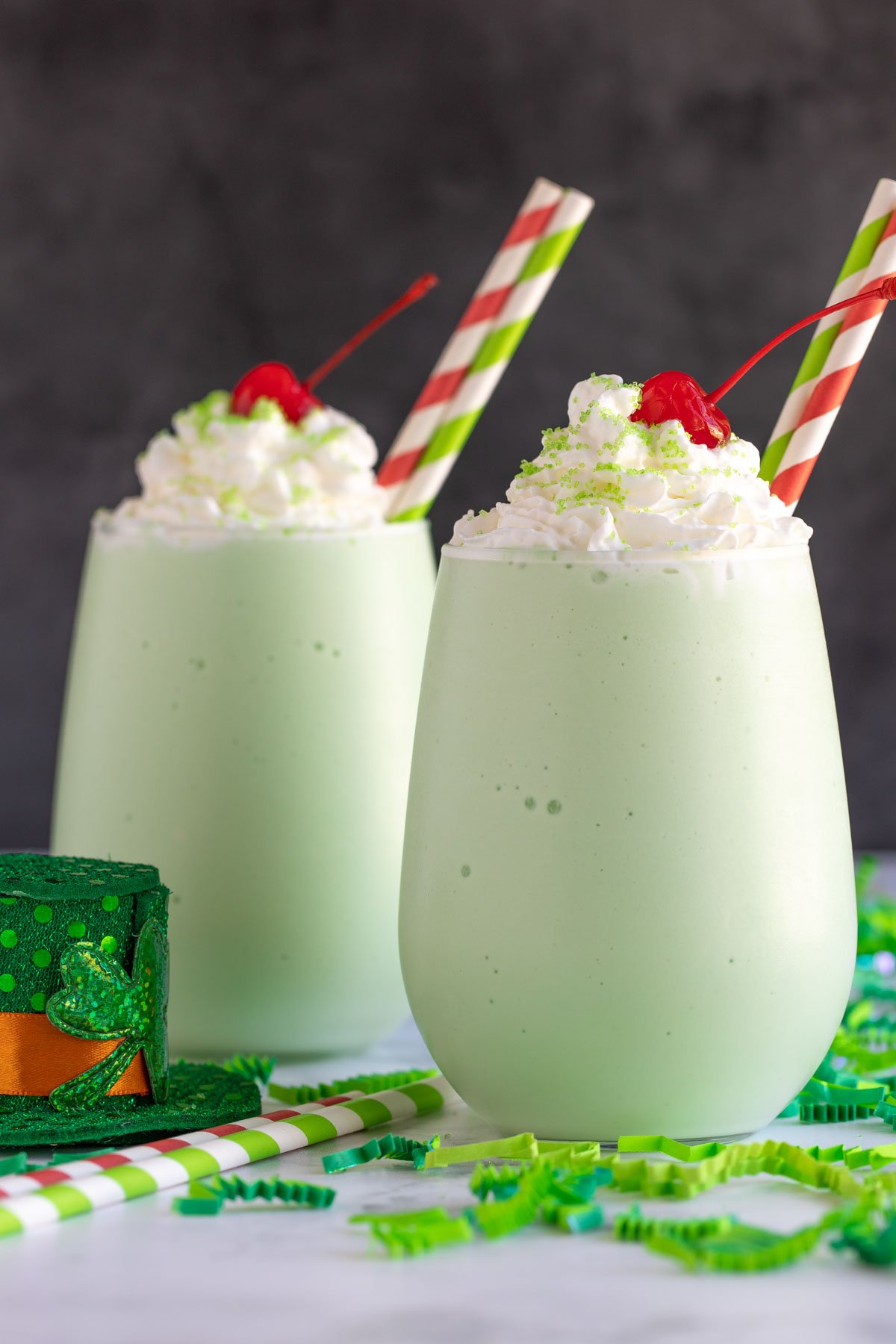 Two boozy shamrock shakes in glasses with red and green striped paper straws.
