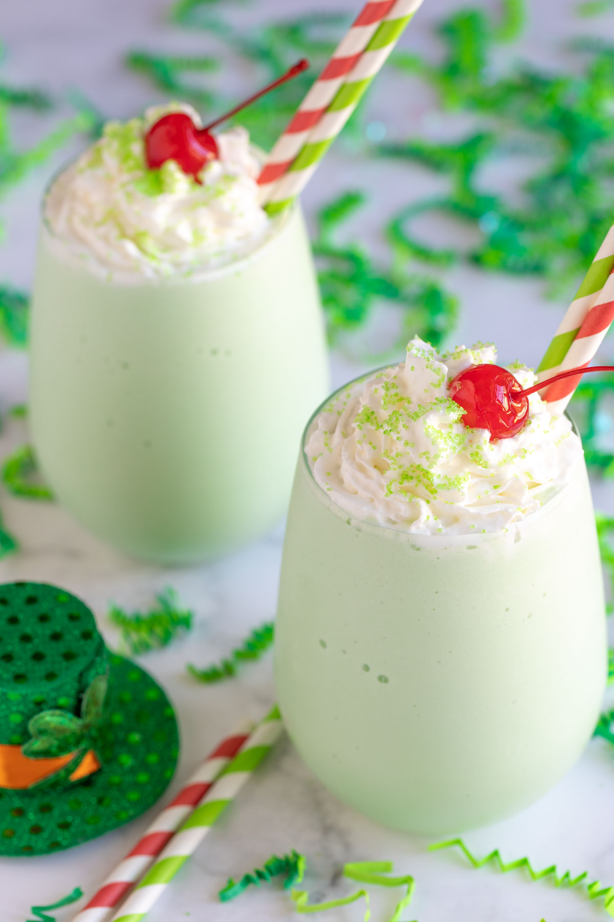 Two boozy shamrock shakes topped with whipped topping, sprinkles and a cherry.