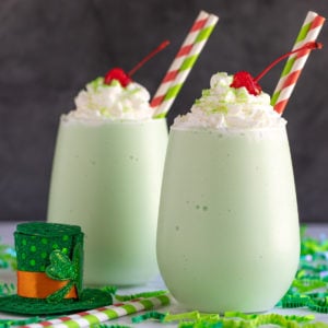 Two boozy shamrock shakes topped with whipped topping, sprinkles and cherries.