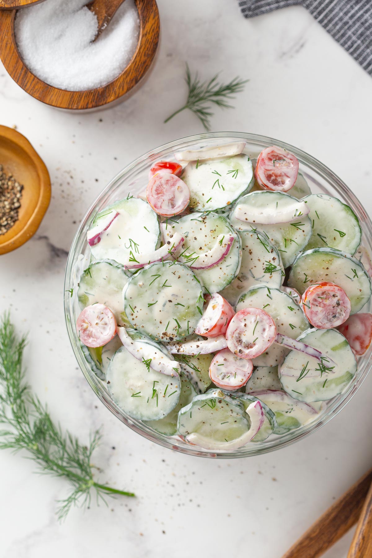 Overhead view of creamy cucumber and tomato salad in a glass bowl.
