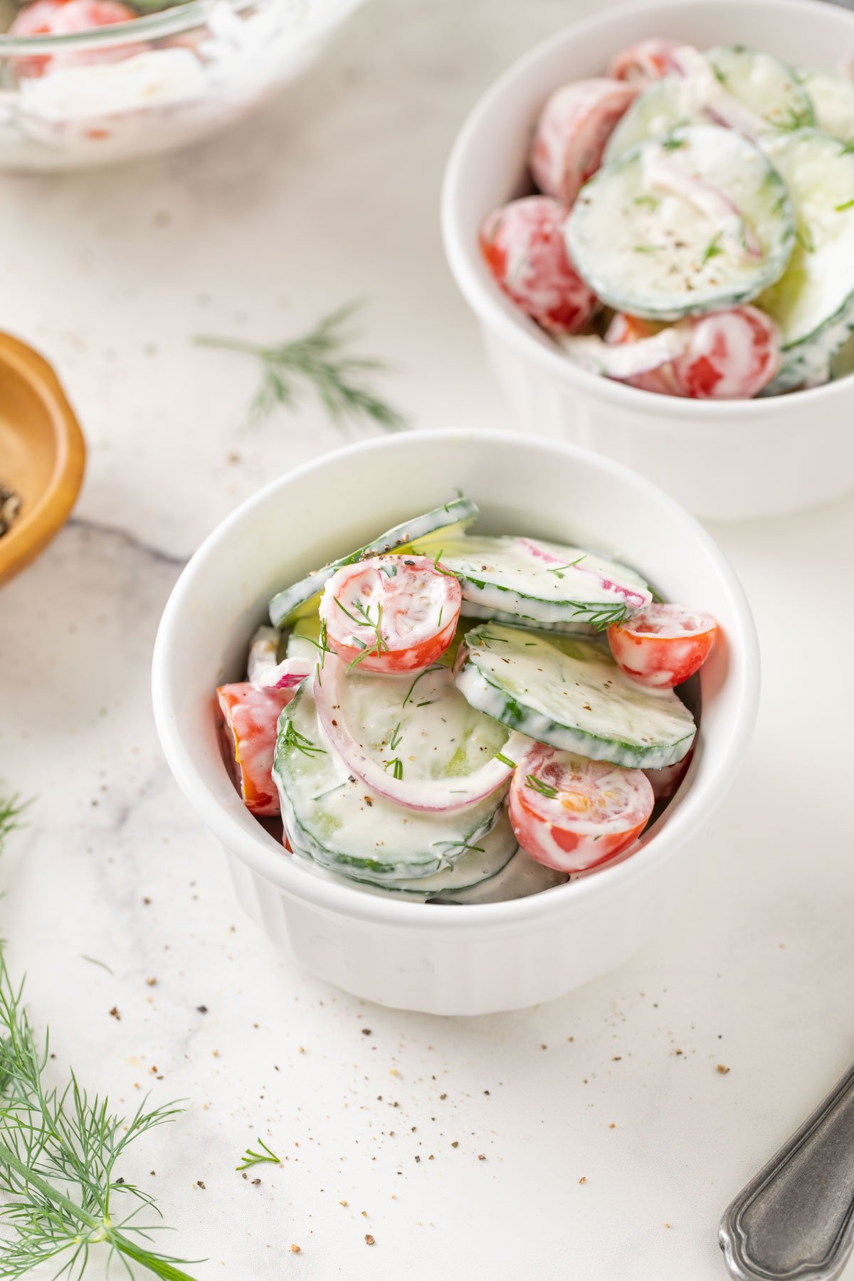 Creamy cucumber and tomato salad with onion in a white ramekin.  