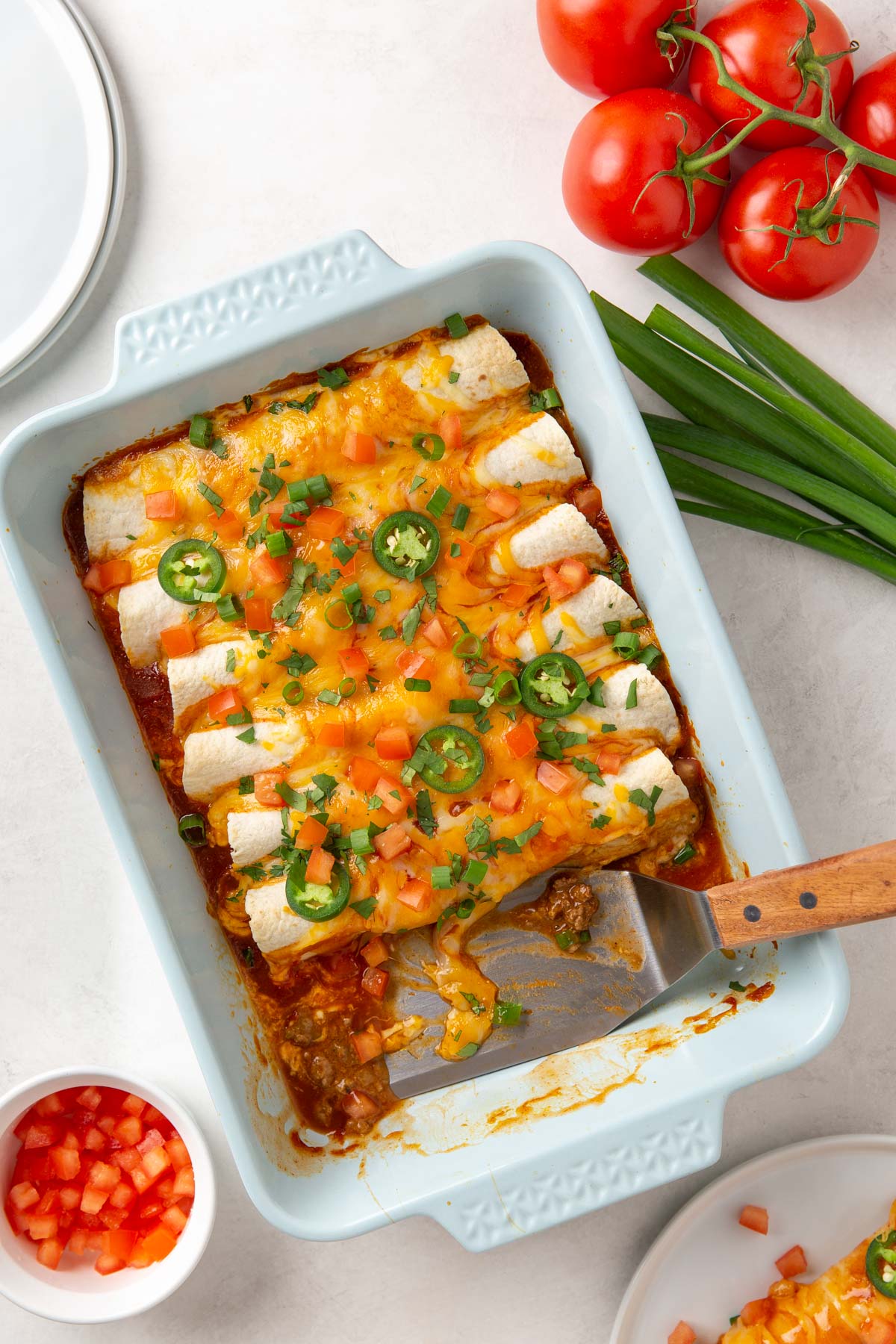A wooden-handled spatula in a baking dish of beef enchiladas.