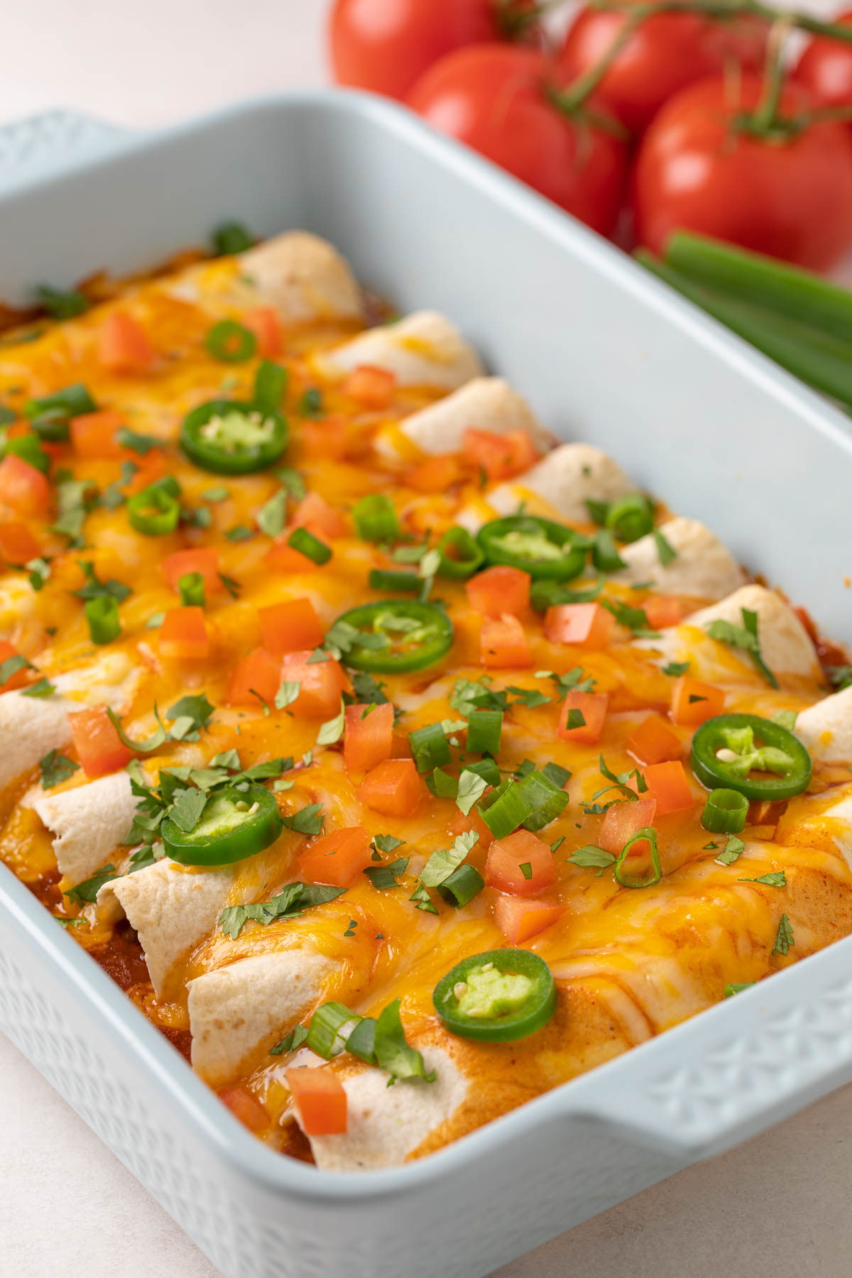 Closeup view of ground beef enchiladas with toppings in a baking dish.