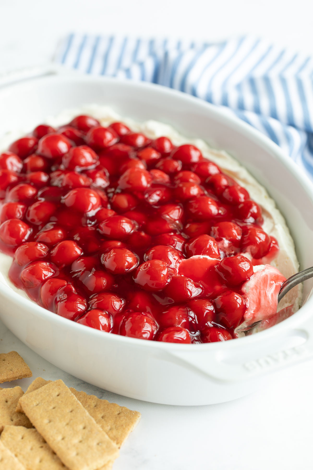 Cherry cheesecake dip in a white baking dish with a spoon.