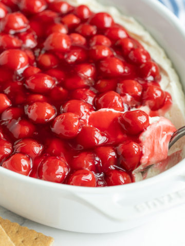 A closeup view of a spoon in a white dish of cherry cheesecake dip.