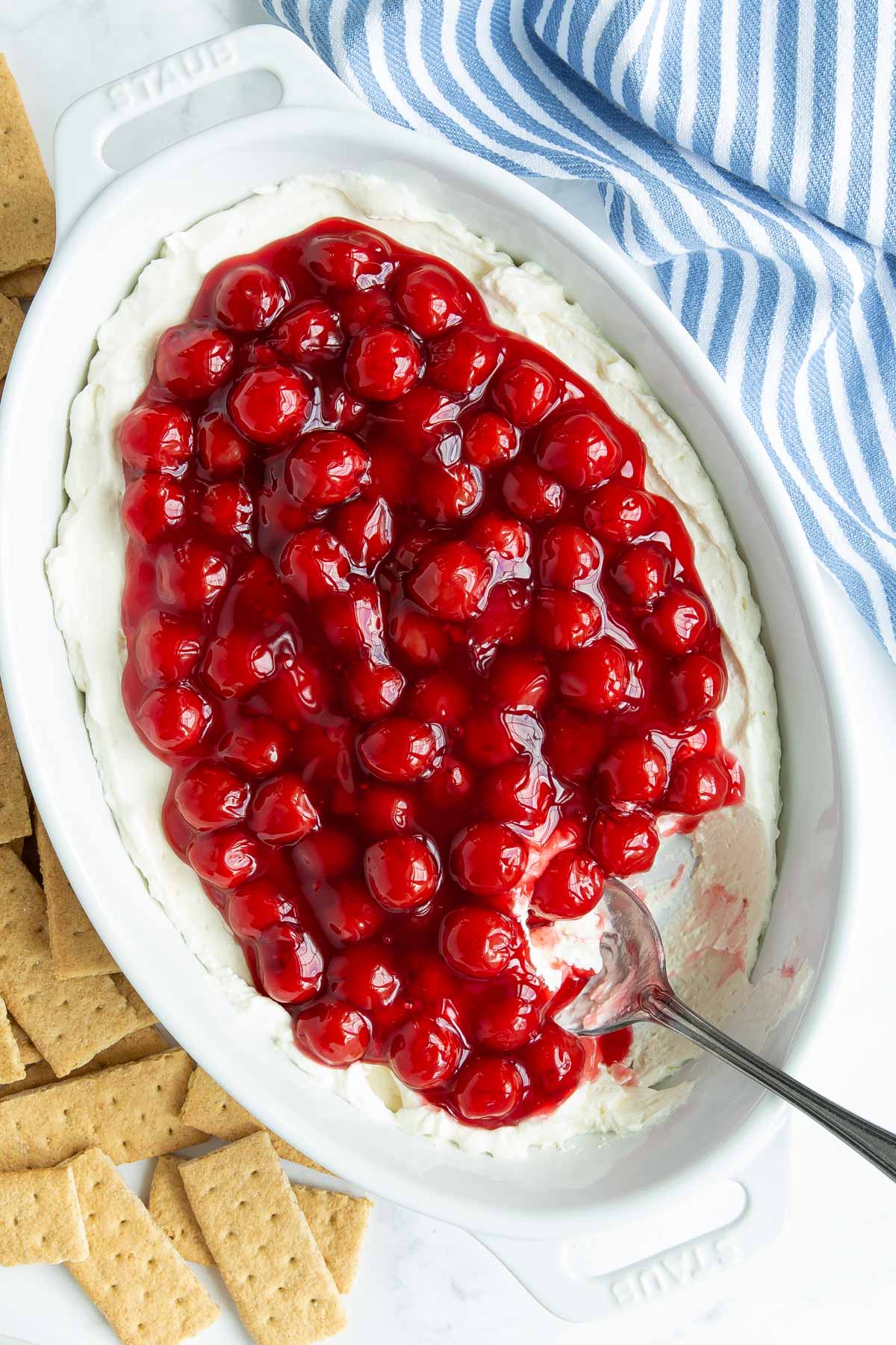 Overhead view of cherry cheesecake dip in an oval white dish with a spoon.