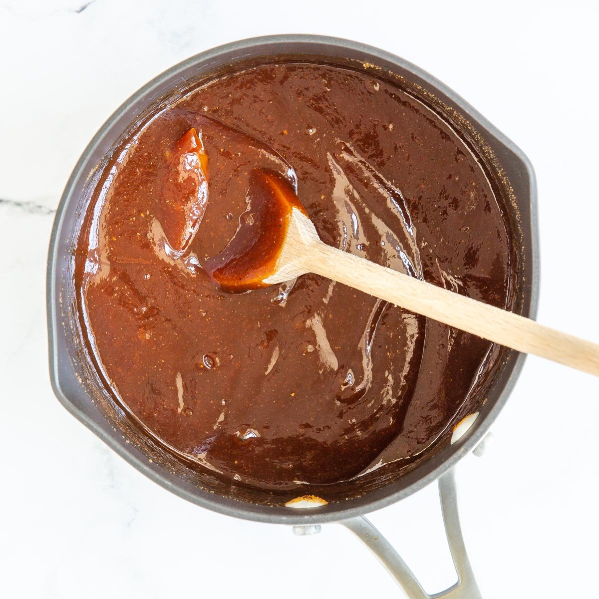 Overhead view of homemade barbecue sauce in a saucepan with a wooden spoon.