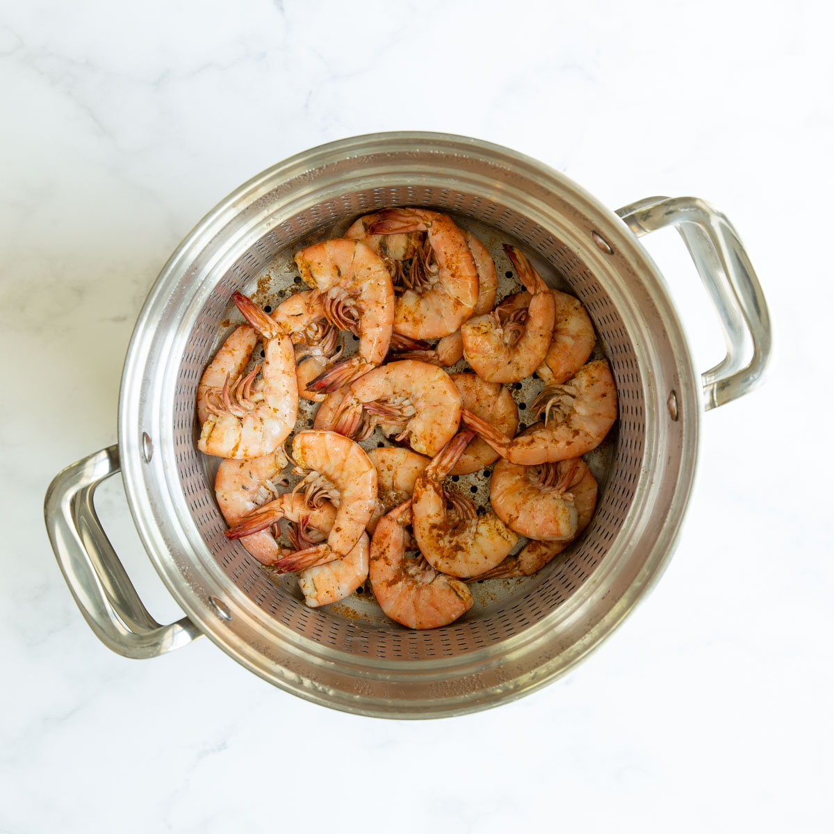 Overhead view of steamed shrimp with old bay in a steamer basket in a pot.