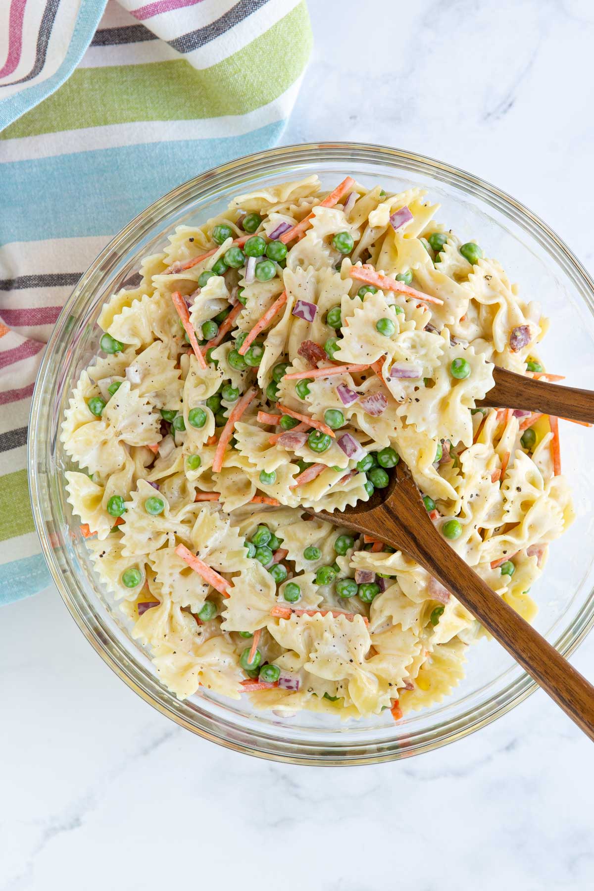 Pea pasta salad with wooden salad servers in a large glass bowl.
