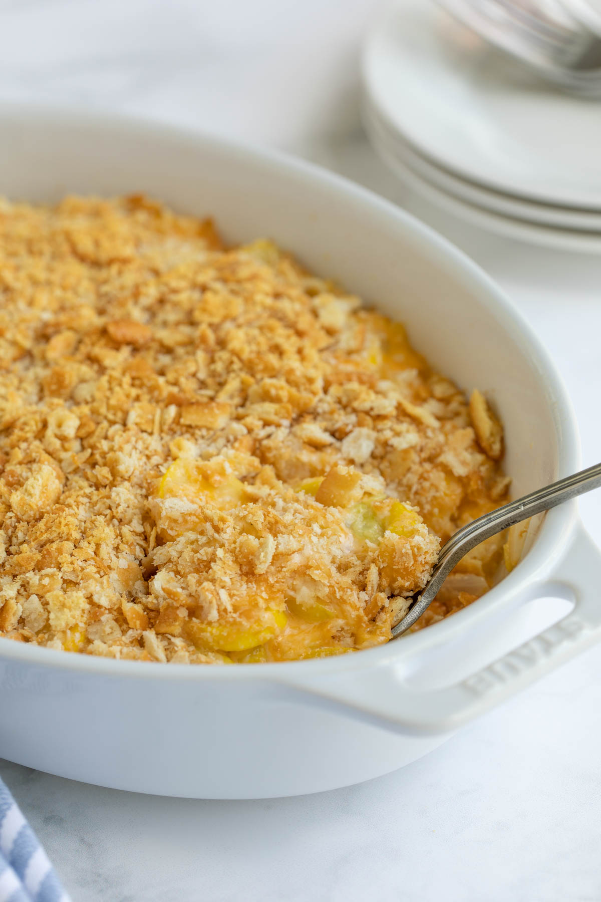 Front view of squash casserole in a white baking dish with a spoon.