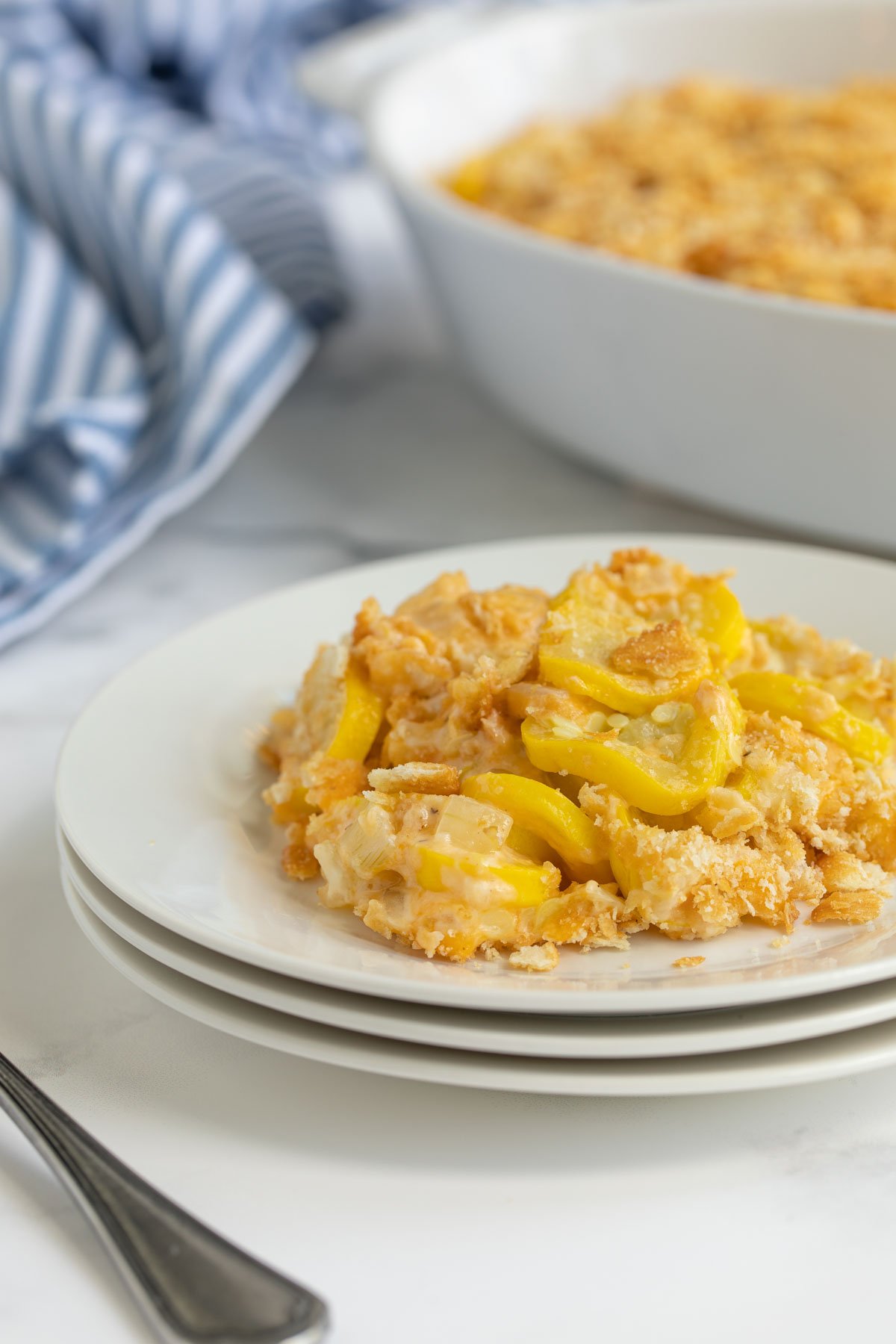 Cheesy squash casserole on a white plate with a baking dish in the background.