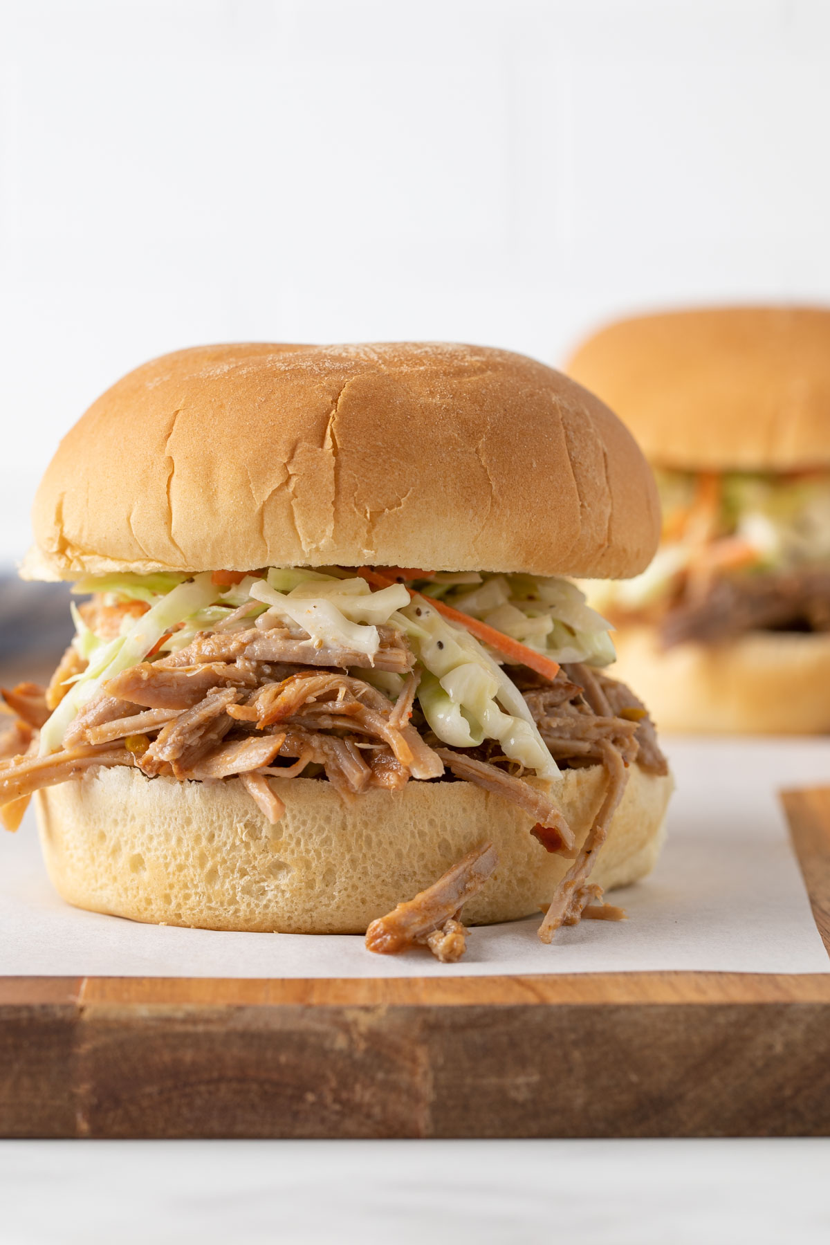 Front closeup view of a pulled pork sandwich on a wood cutting board.