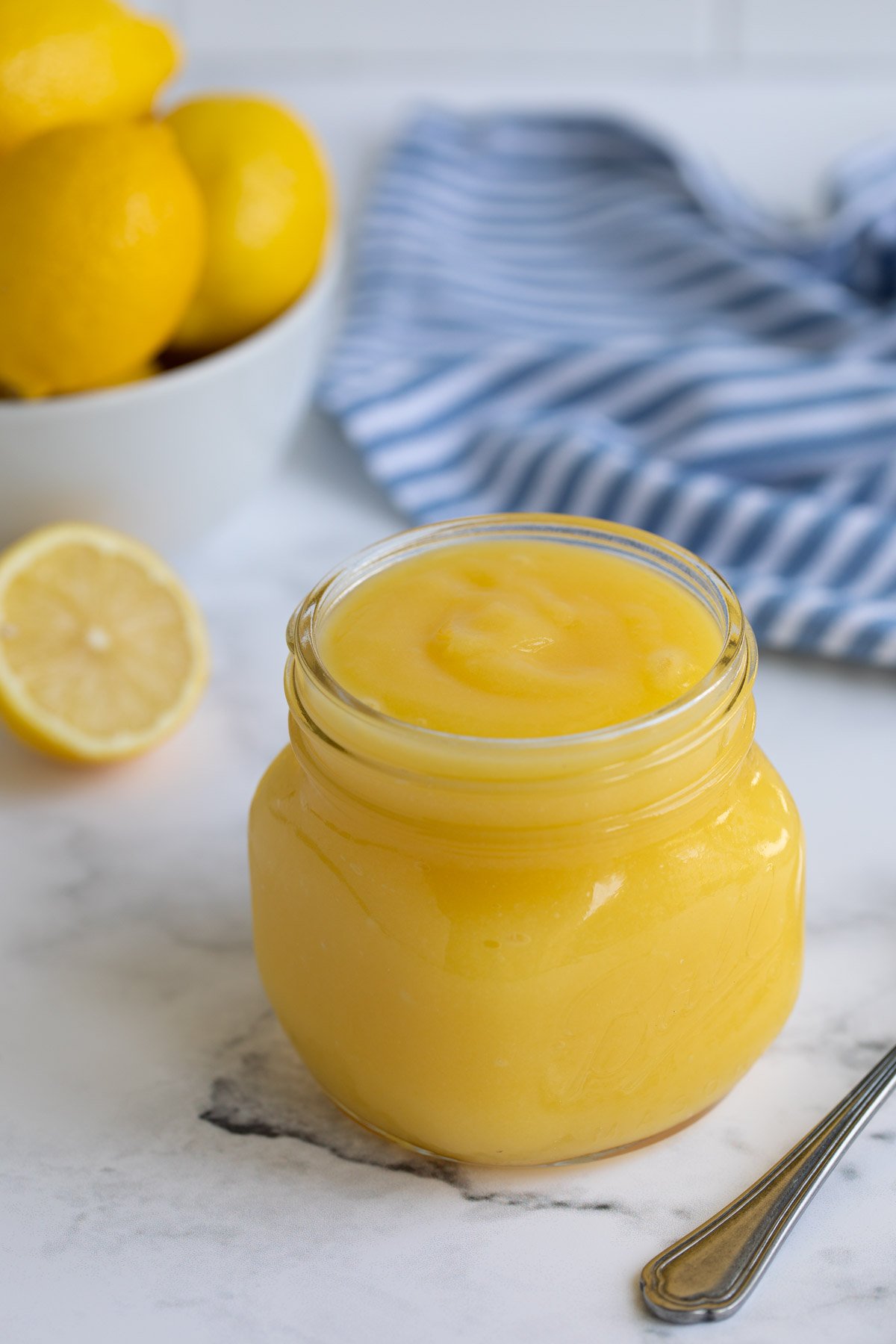 A jar of microwave lemon curd by a bowl of lemons and a striped towel.