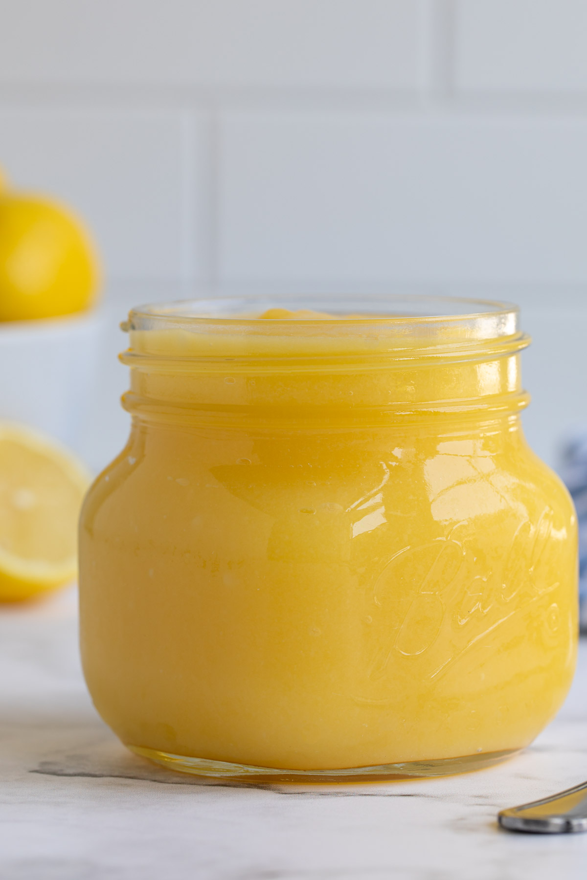 Front view of a pint jar of lemon curd by a spoon.