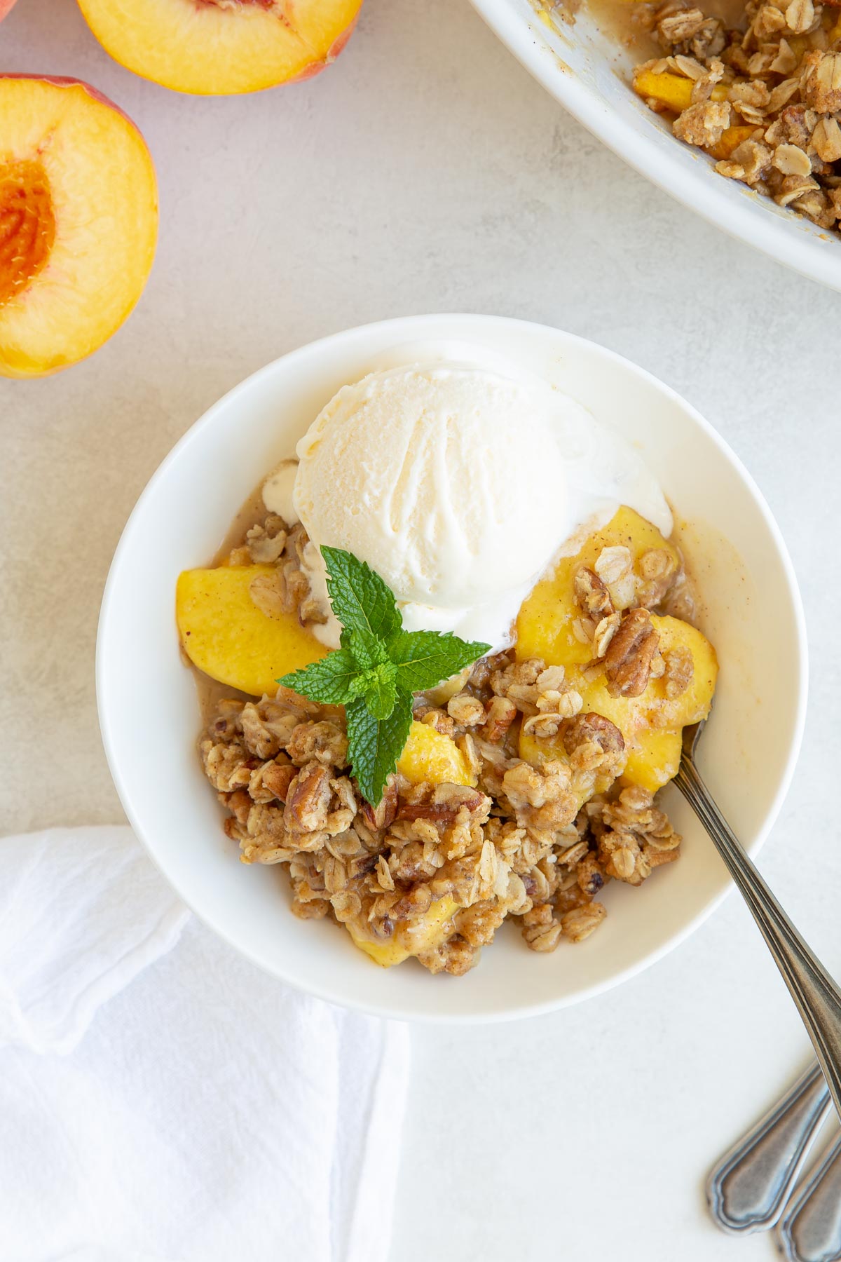 Overhead view of a bowl of peach crisp topped with a scoop of ice cream.