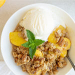 A bowl of fruit crisp topped with ice cream. Overlay text reads "Peach Crisp".
