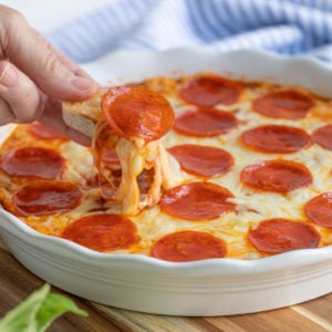 A French baguette slice being dipped into baked pepperoni pizza dip.