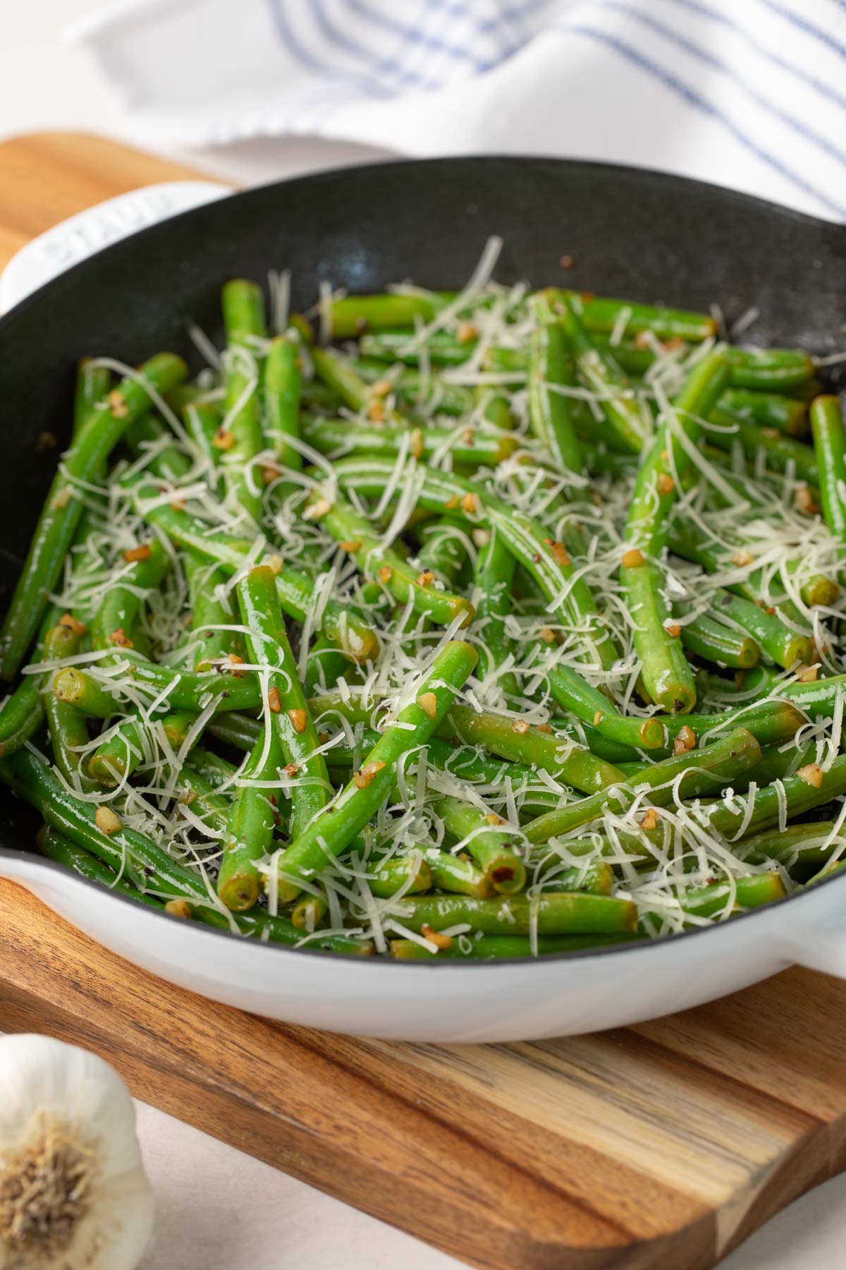 Closeup view of sauteed beans with garlic and Parmesan in a white skillet.