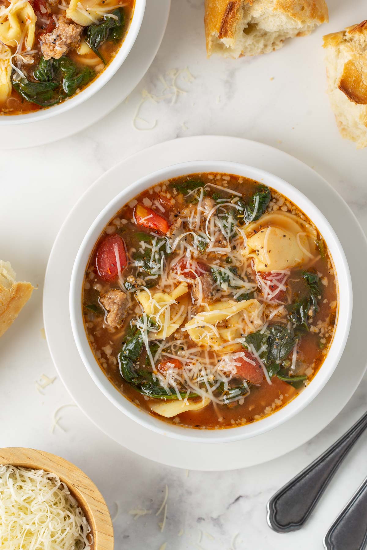 Overhead view of Italian sausage and tortellini soup with spinach in a white bowl.