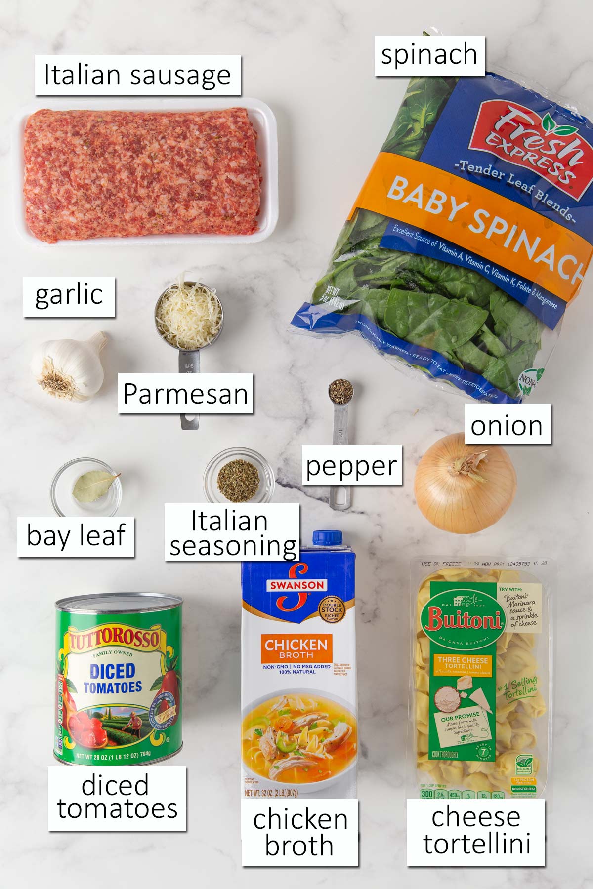 Ingredients needed to make tortellini soup on a white marble surface.