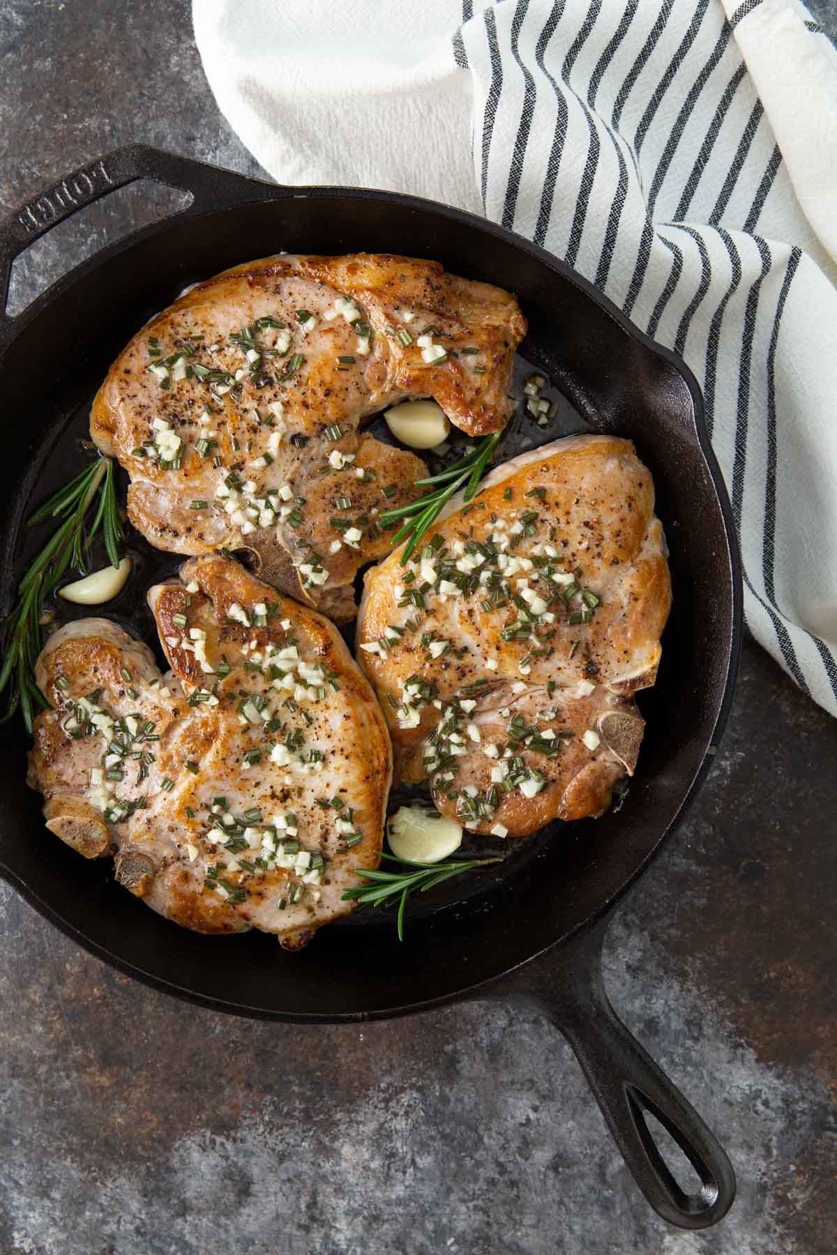 Overhead view of baked rosemary chops with garlic in a cast iron skillet.