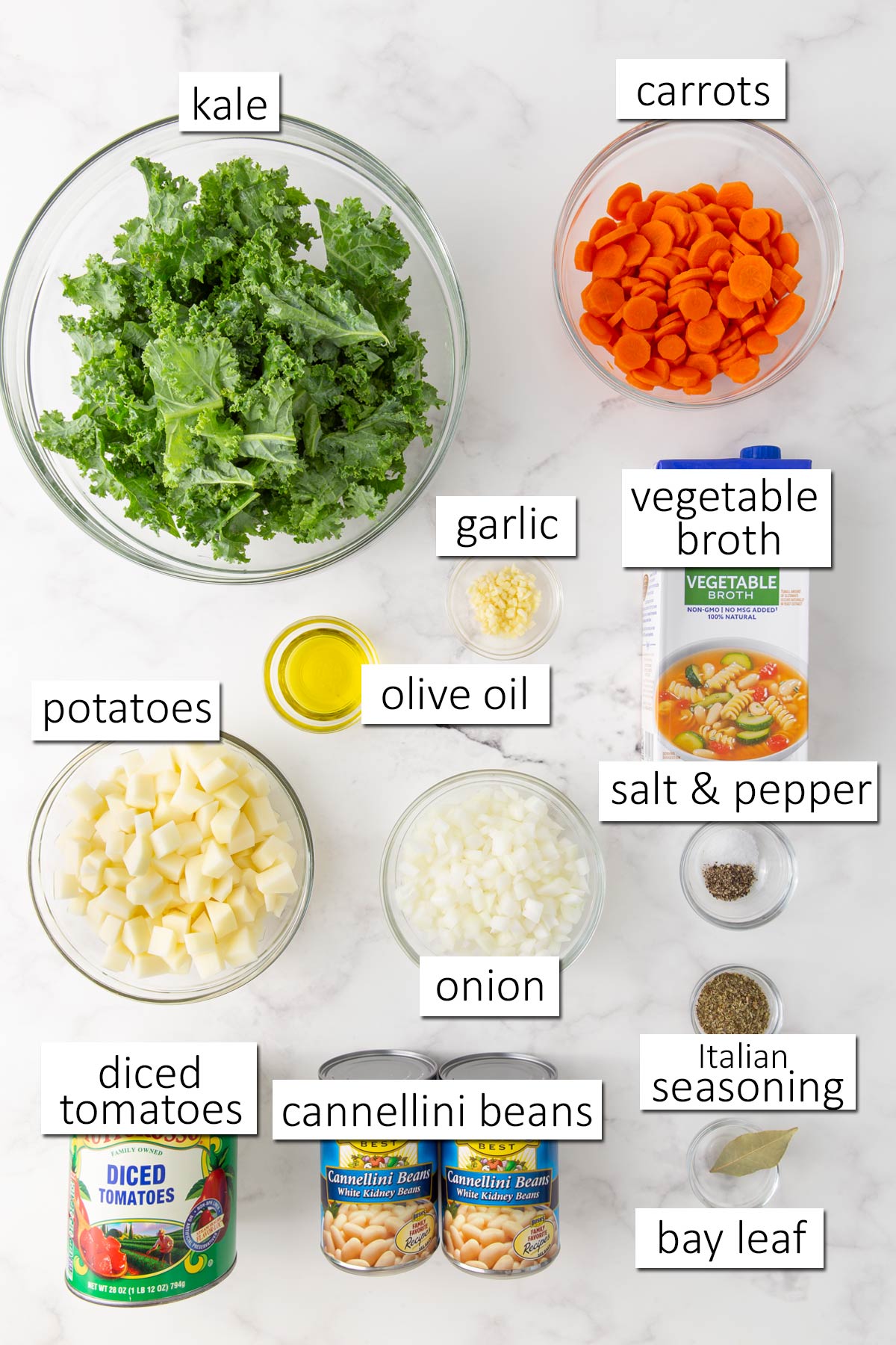 Overhead view of ingredients for kale soup on a white marble surface.