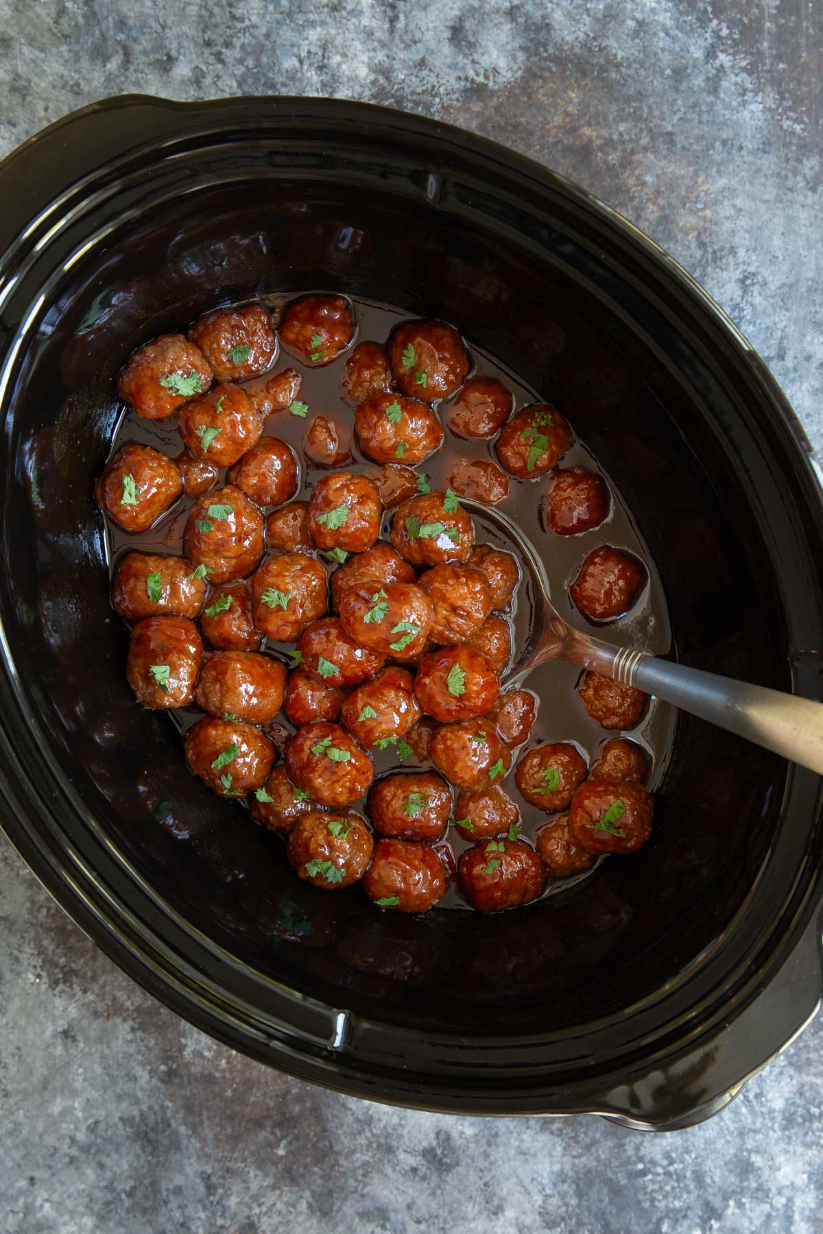 Overhead view of grape jelly meatballs in an oval crock pot.