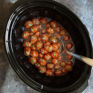 Overhead view of grape jelly meatballs in a crock pot with a ladle.