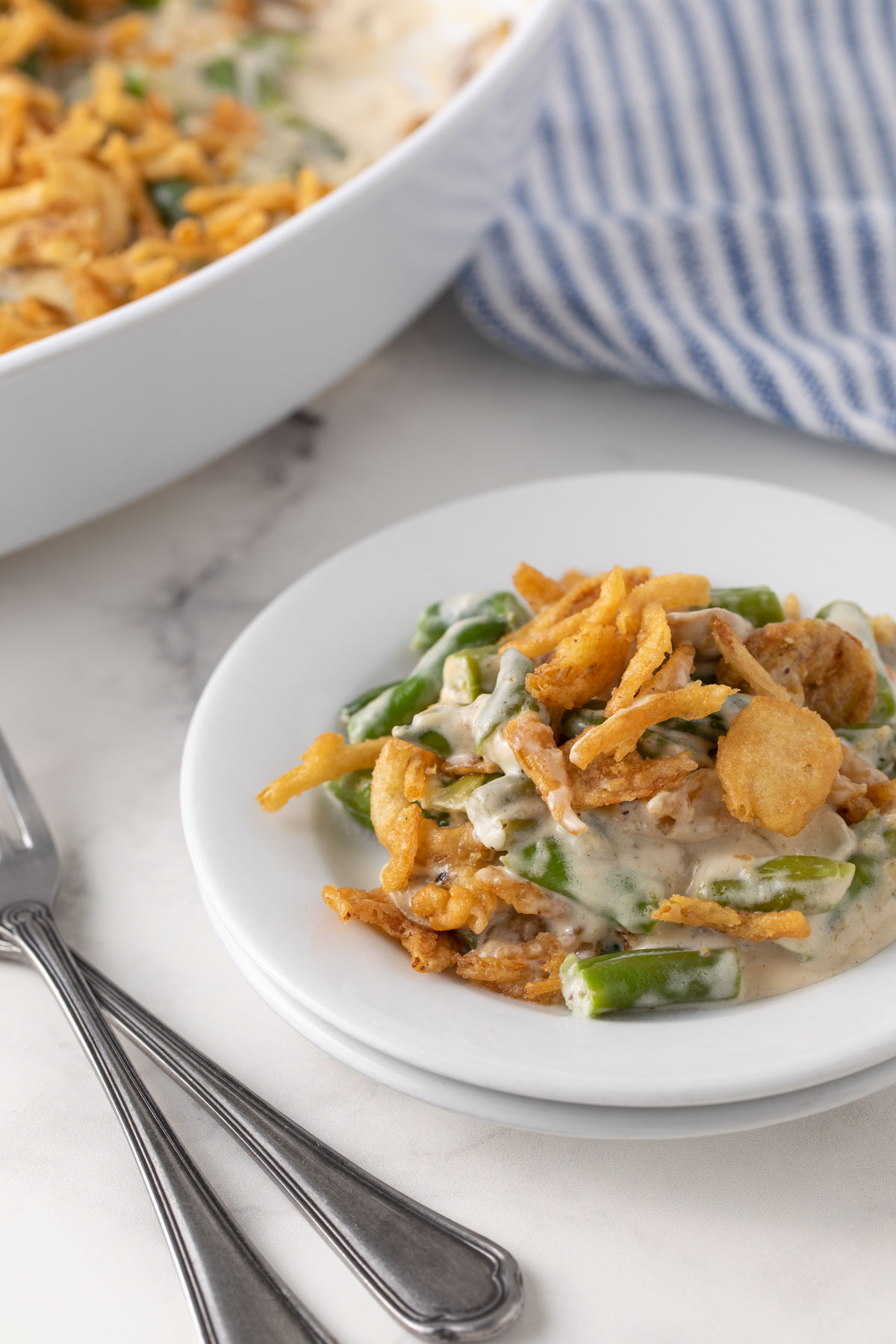 Green bean casserole on a round white plate beside two forks.