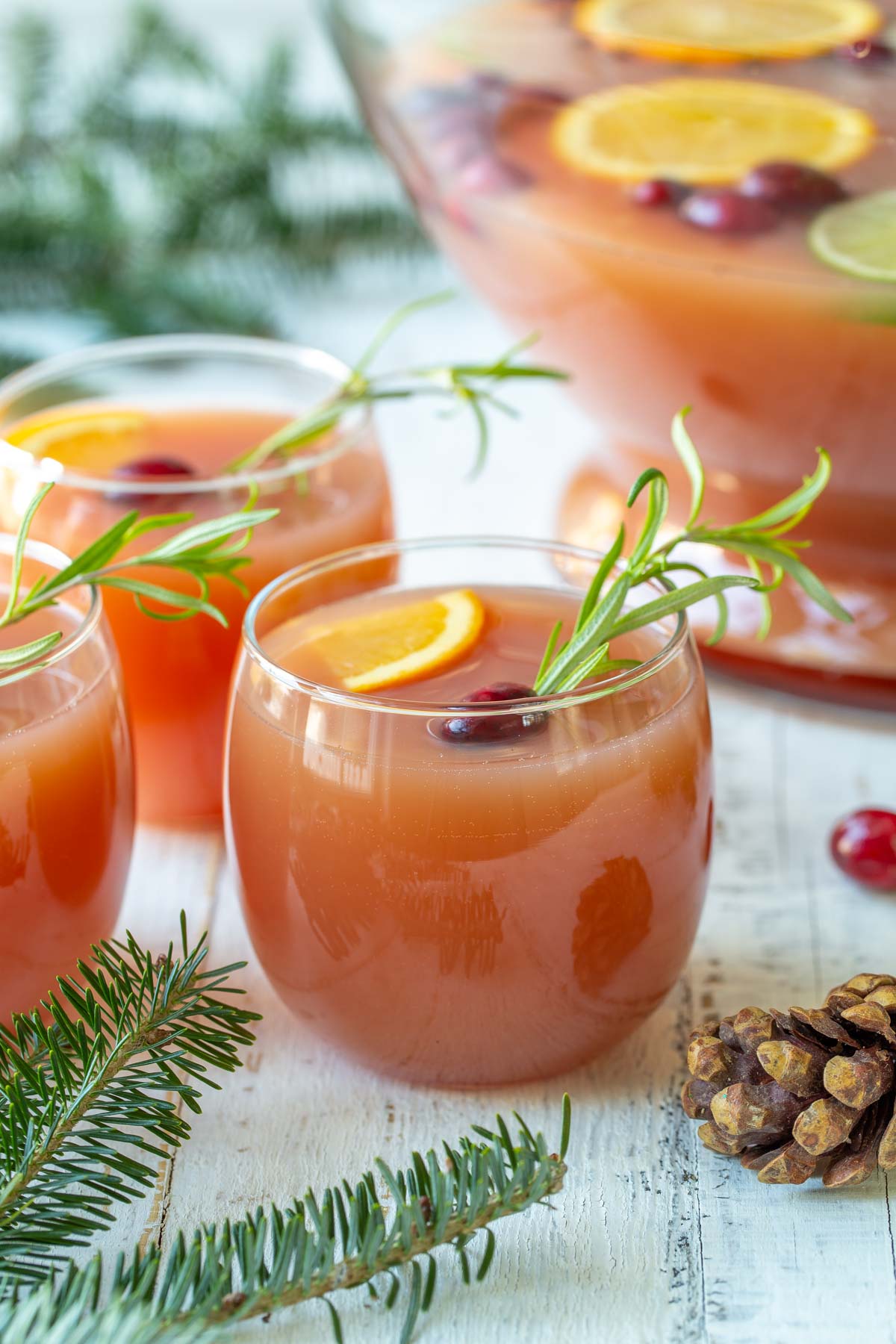 Front view of three garnished glasses of Christmas punch.  A punch bowl is in the background.