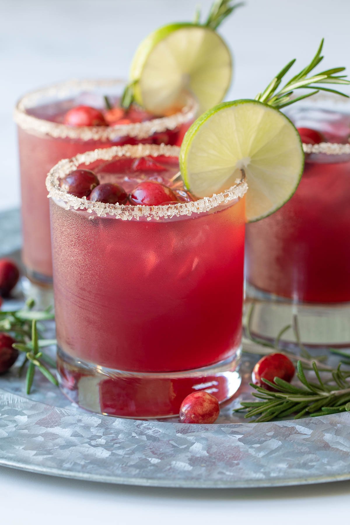 Front view of three cranberry margaritas garnished with cranberries, lime and rosemary.
