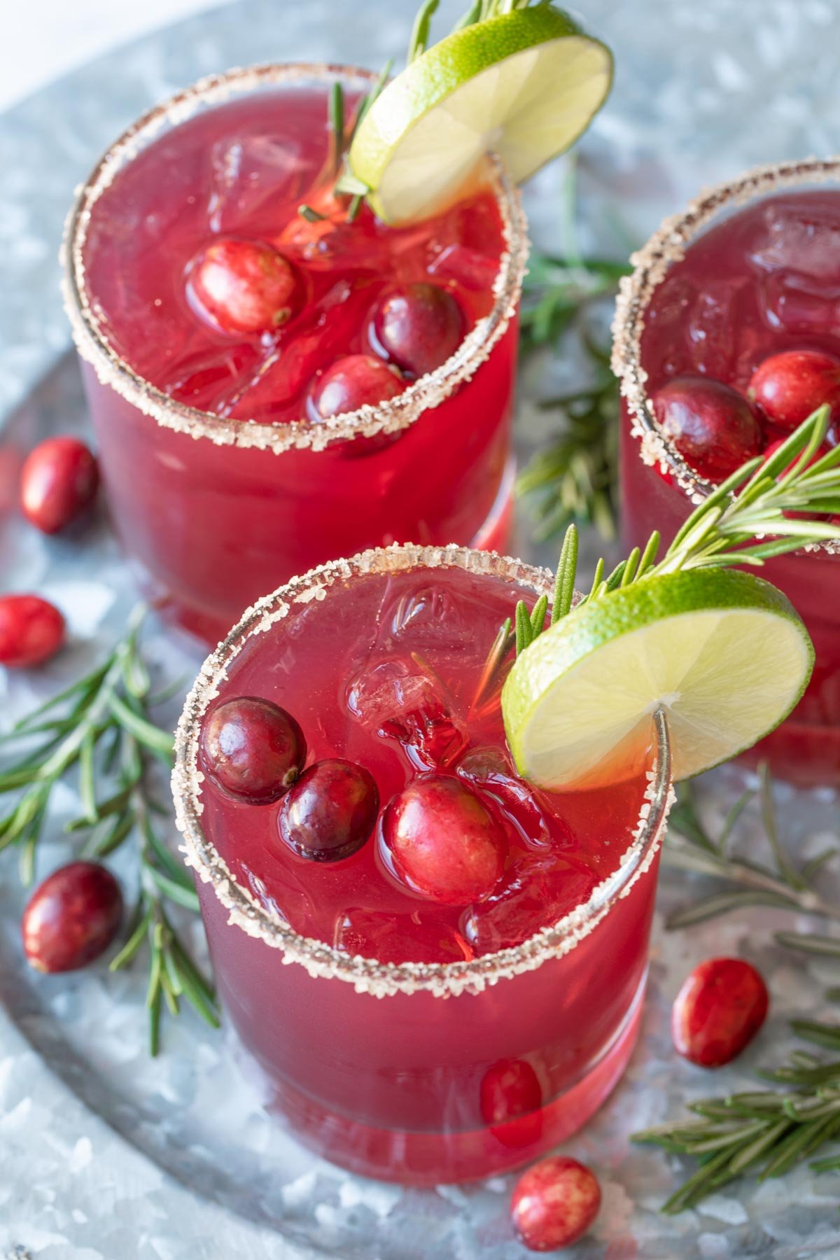 Three garnished cranberry margaritas on a silver serving tray.