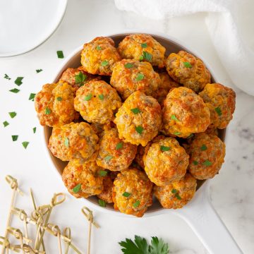 Sausage cheese balls sprinkled with parsley in a white serving dish.