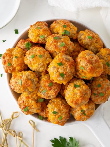 Sausage cheese balls sprinkled with parsley in a white serving dish.
