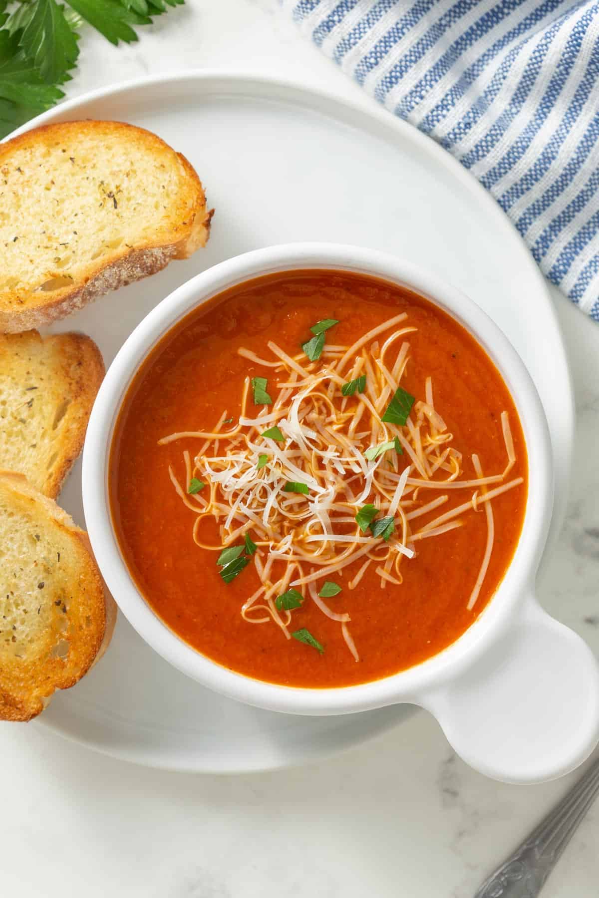 Overhead view of easy tomato soup in a white bowl beside three slices of French bread.  