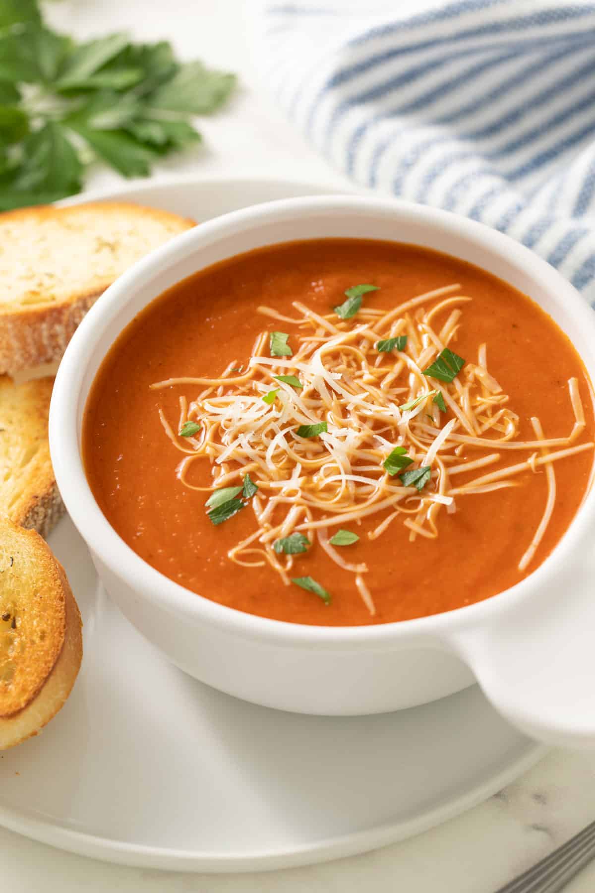 Closeup view of a bowl of tomato soup topped with Parmesan cheese and parsley.  