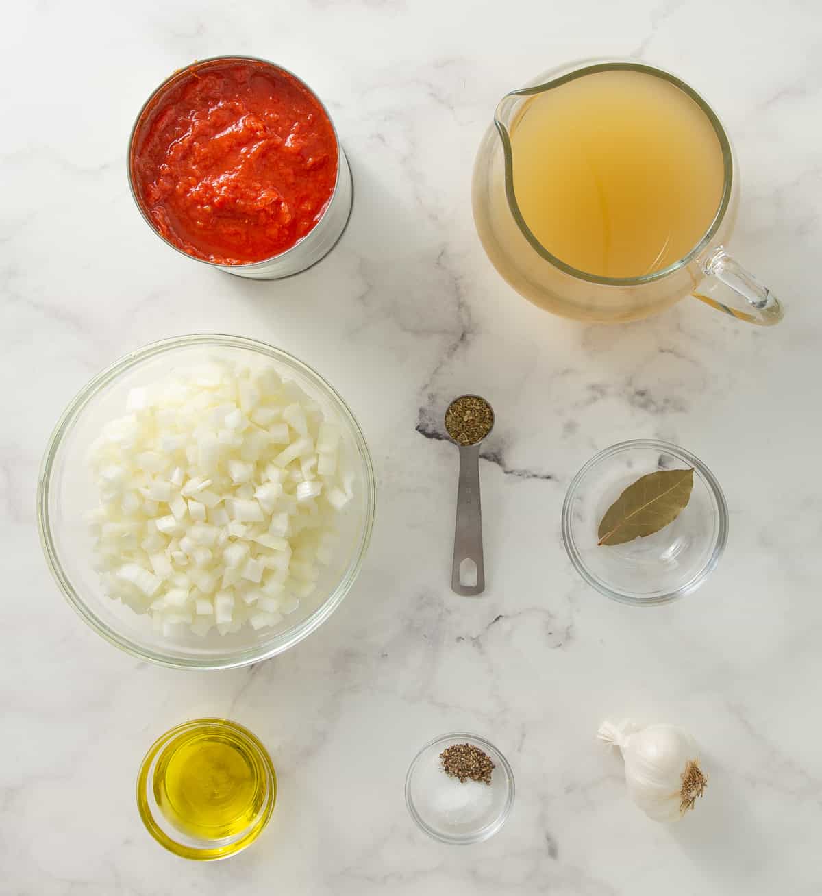 Overhead view of ingredients for tomato soup on a white marble surface.