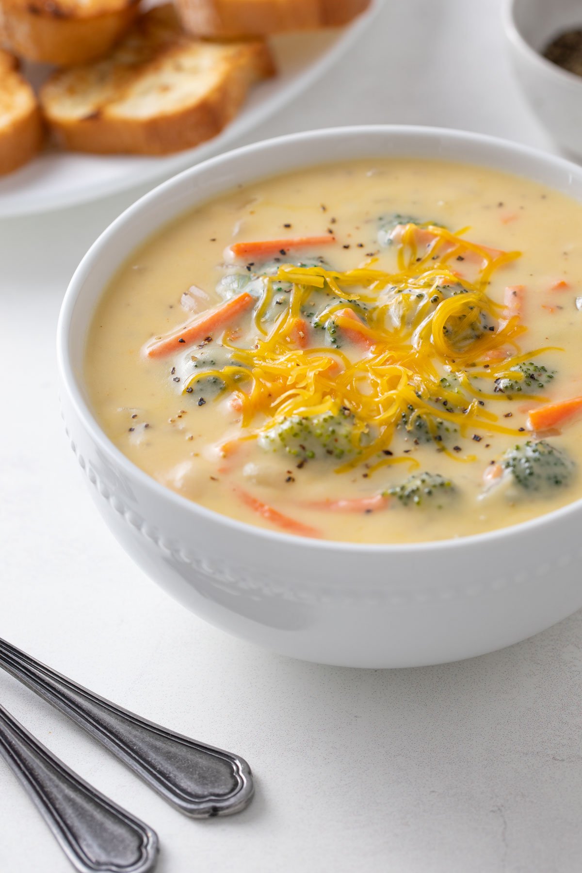 A white bowl of low fat broccoli cheese soup topped with shredded cheese.