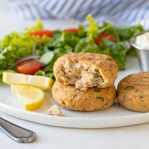 Three air fryer salmon patties on a plate with a salad.