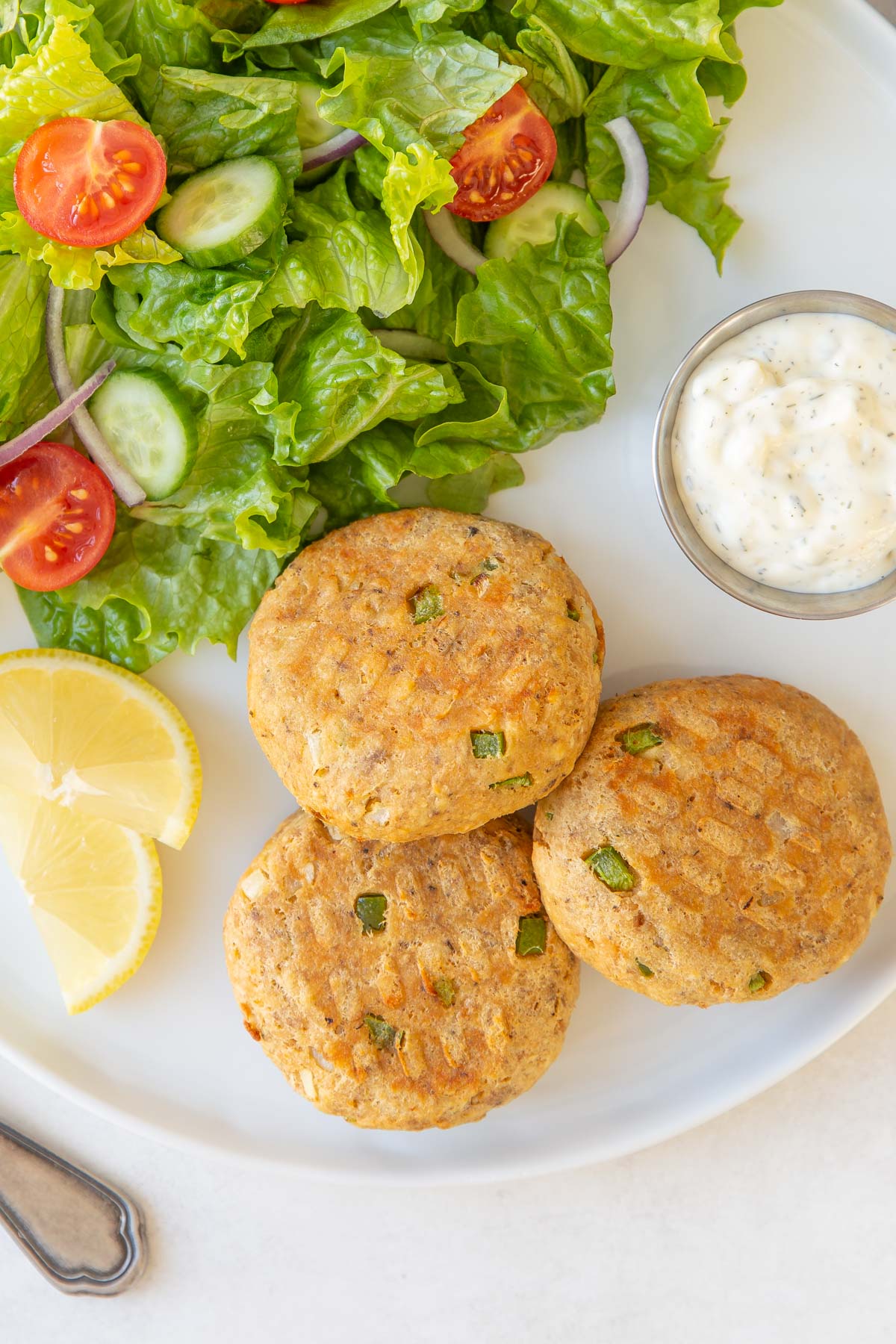 Overhead view of three salmon patties on a plate with a salad and tartar sauce.
